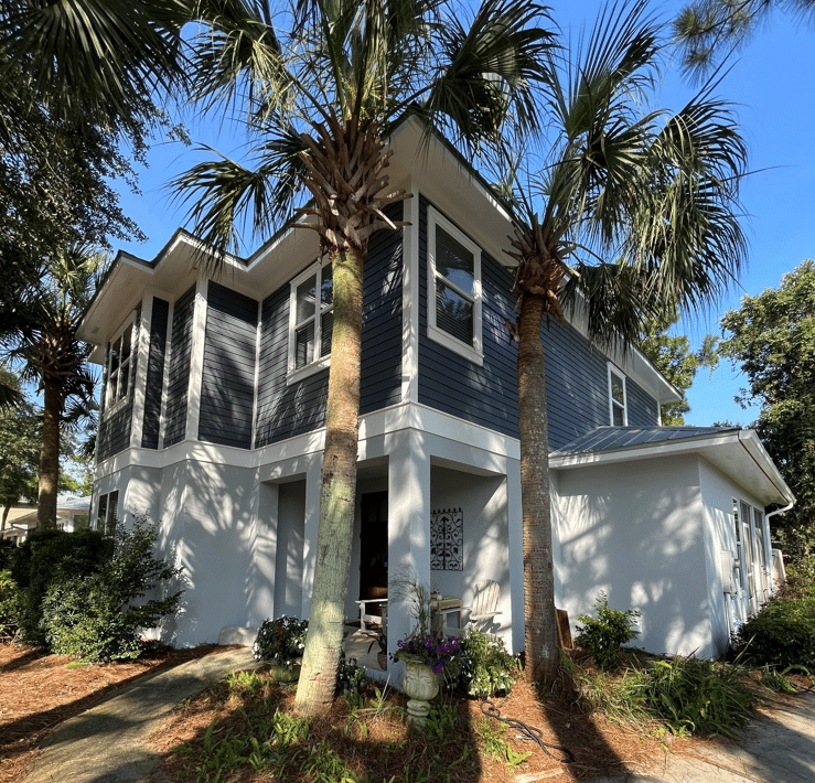 Two-story home we painted matte gray and white in Miramar Beach sitting behind two palm trees.